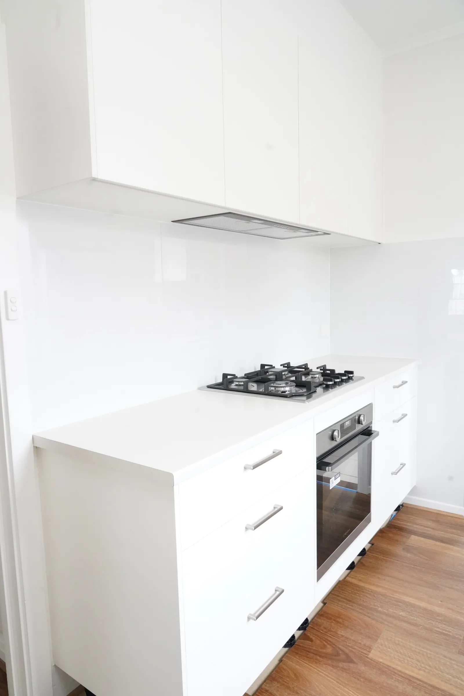 New white kitchen with a gas cooktop, built-in oven and timber flooring
