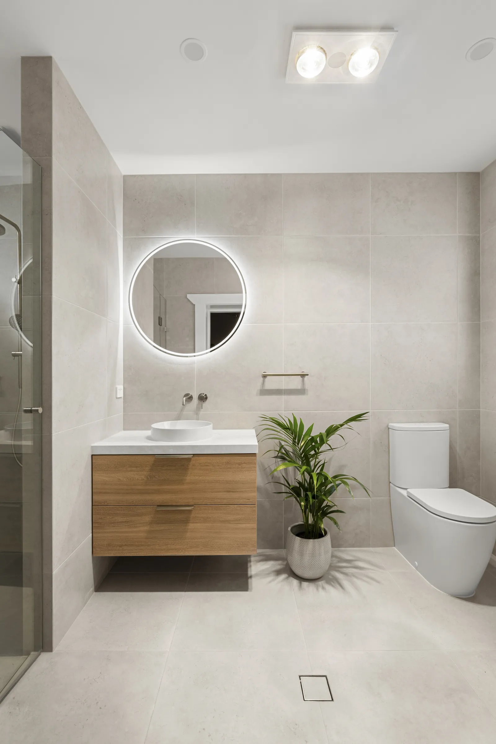 Ensuite with a floating timber-look vanity, backlit round mirror and large-format grey tiles